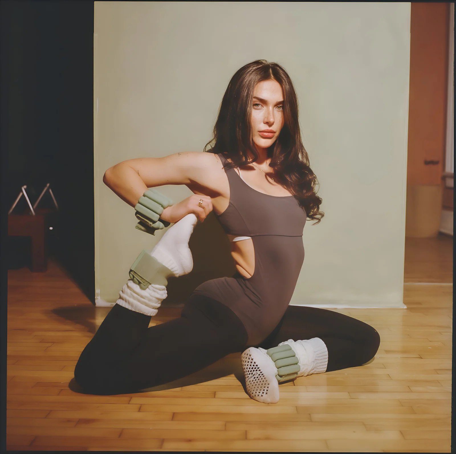 Julianna seated on a wooden floor in a movement pose, looking toward the camera